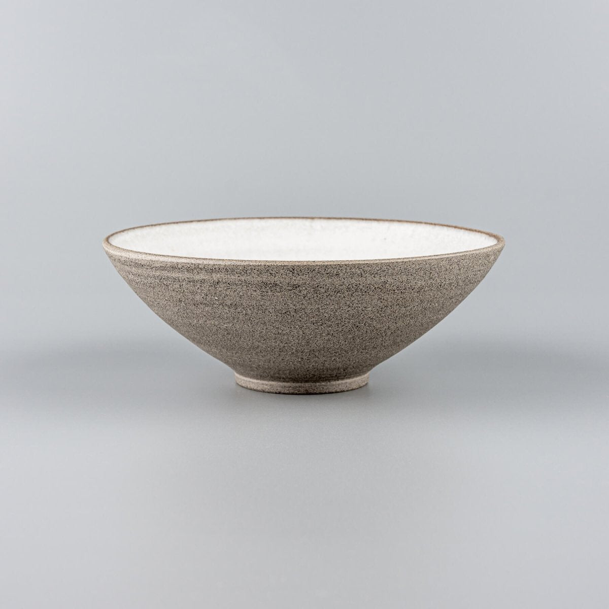 Handmade ceramic bowl with raw stoneware exterior and white glazed interior for modern restaurant settings.
