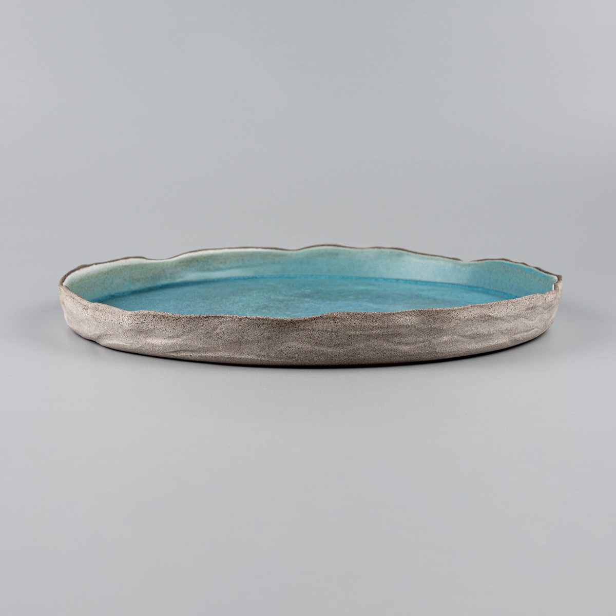 Elegant turquoise handmade dinner plate with textured unglazed exterior for premium culinary presentation.