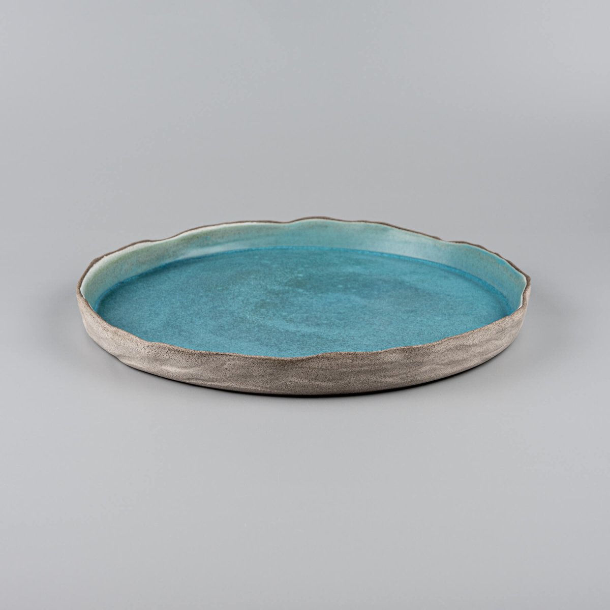 Side view of handmade dinner plate in ocean-inspired turquoise with refined beveled edges.