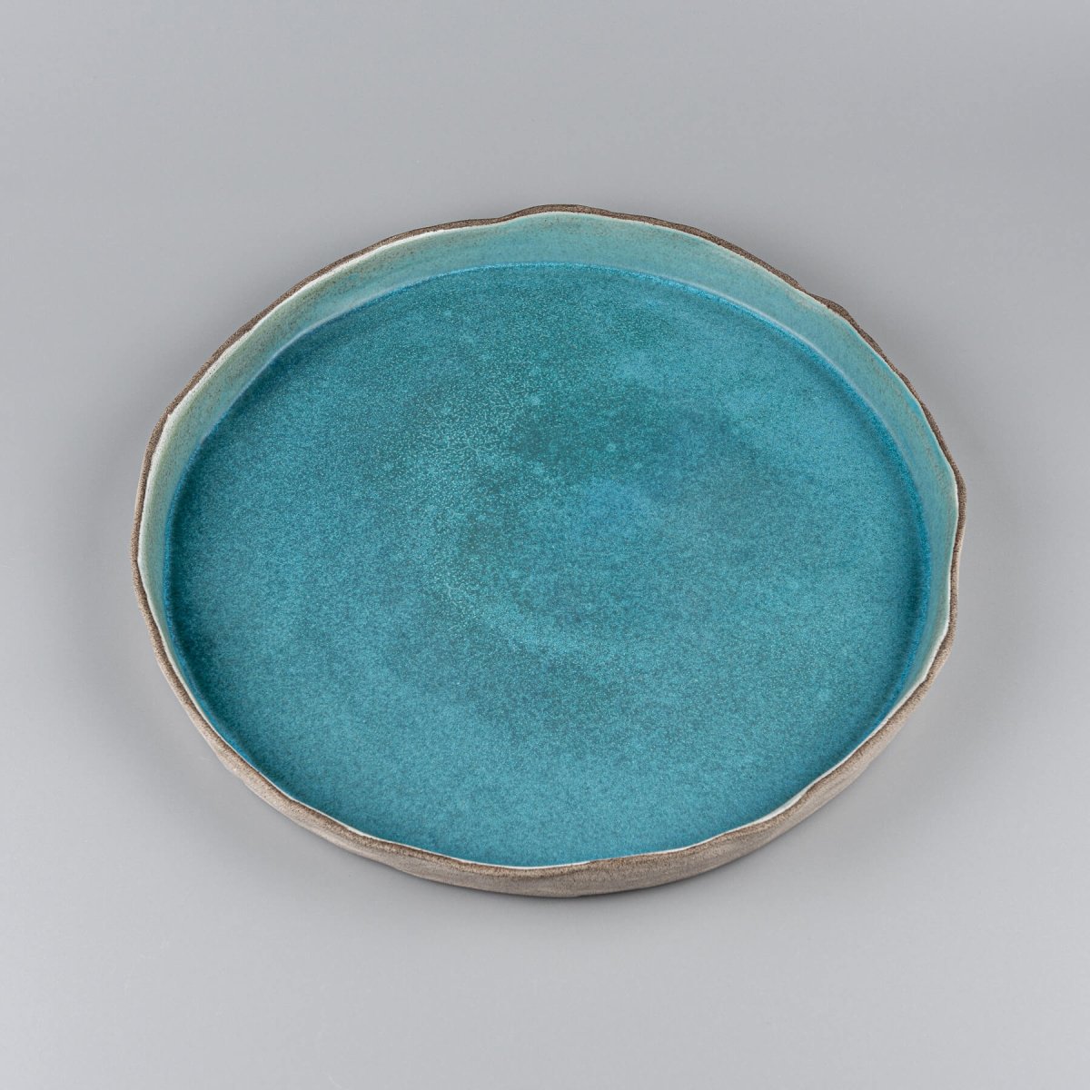 Close-up of turquoise handmade dinner plate with artistic wave-like edge detail for luxury restaurants.