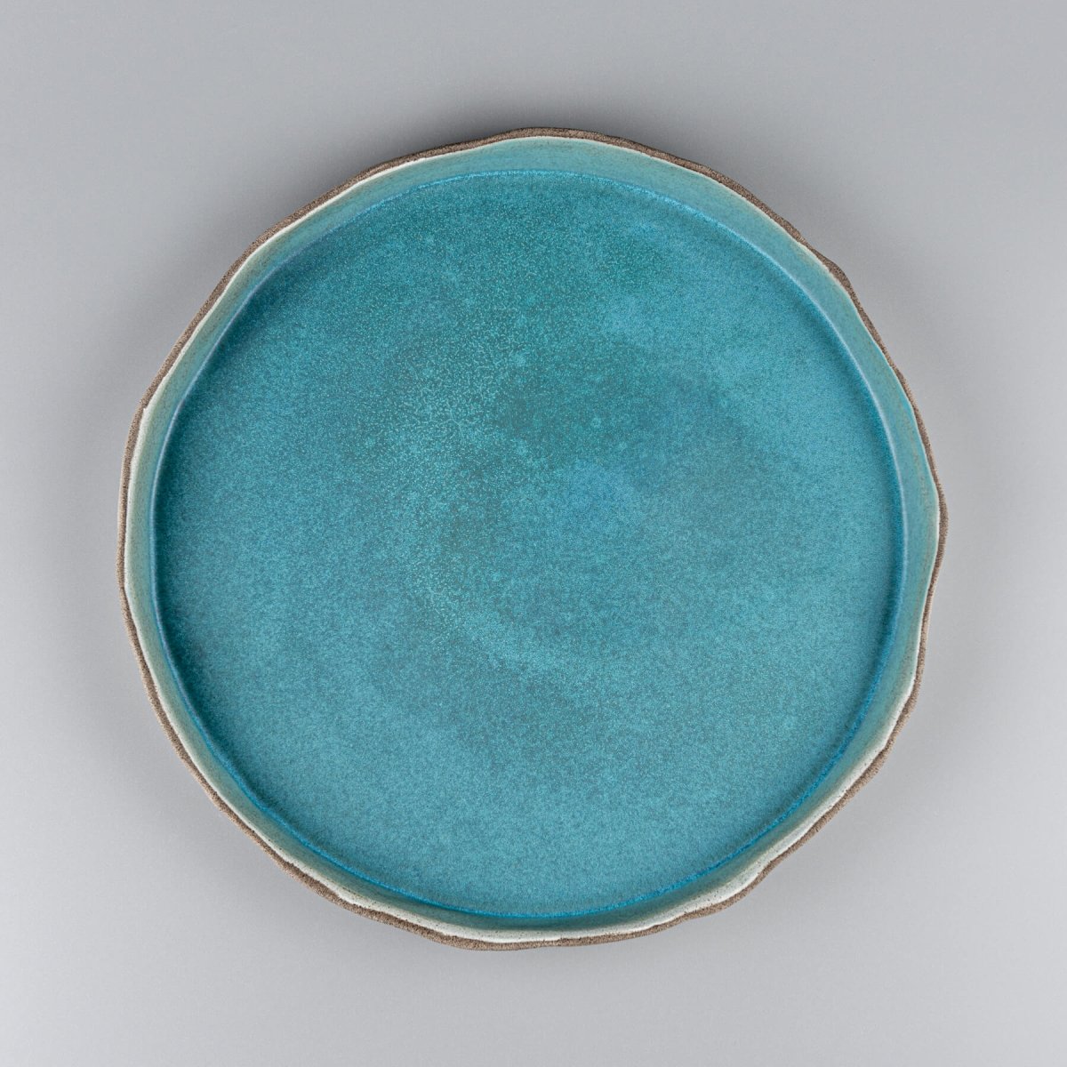 Handmade dinner plate in matte turquoise with wave-like white edges for fine dining and luxury tableware.