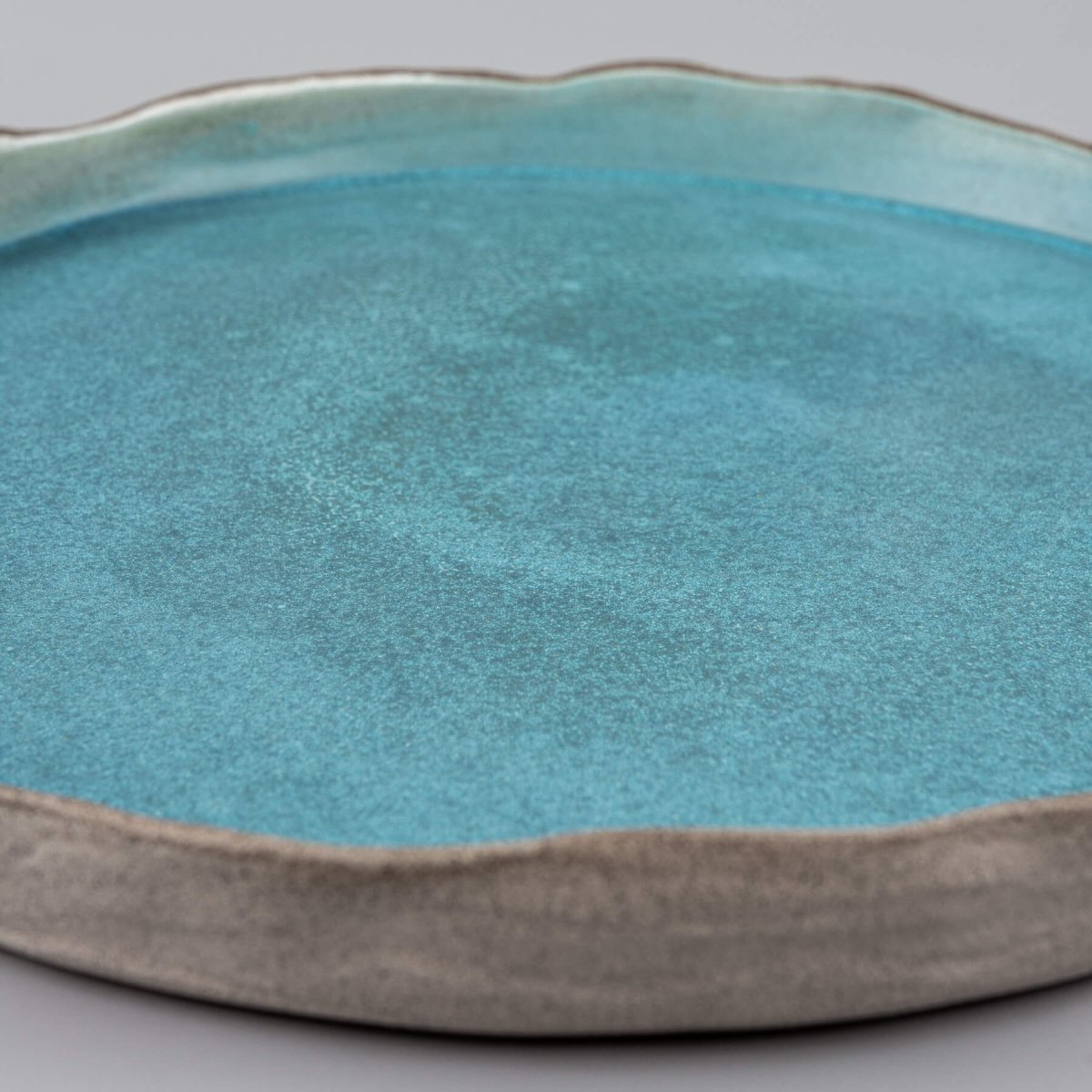 Detail of handmade dinner plate edge with organic wave form and subtle white accent for fine dining.