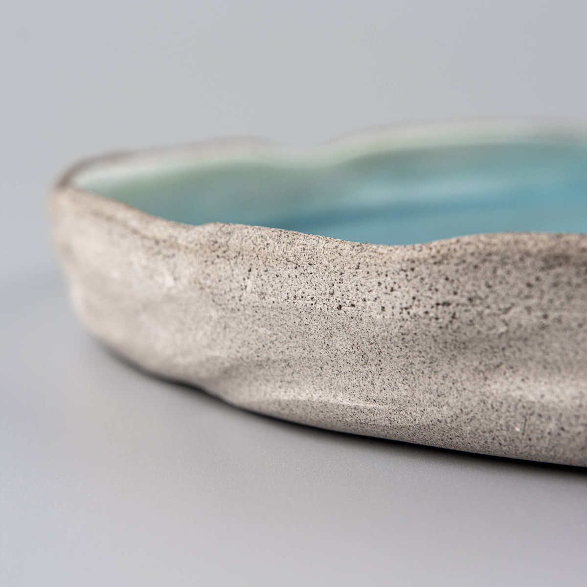 Handmade dinner plate with unglazed textured stoneware exterior and matte turquoise glazed interior for luxury fine dining.