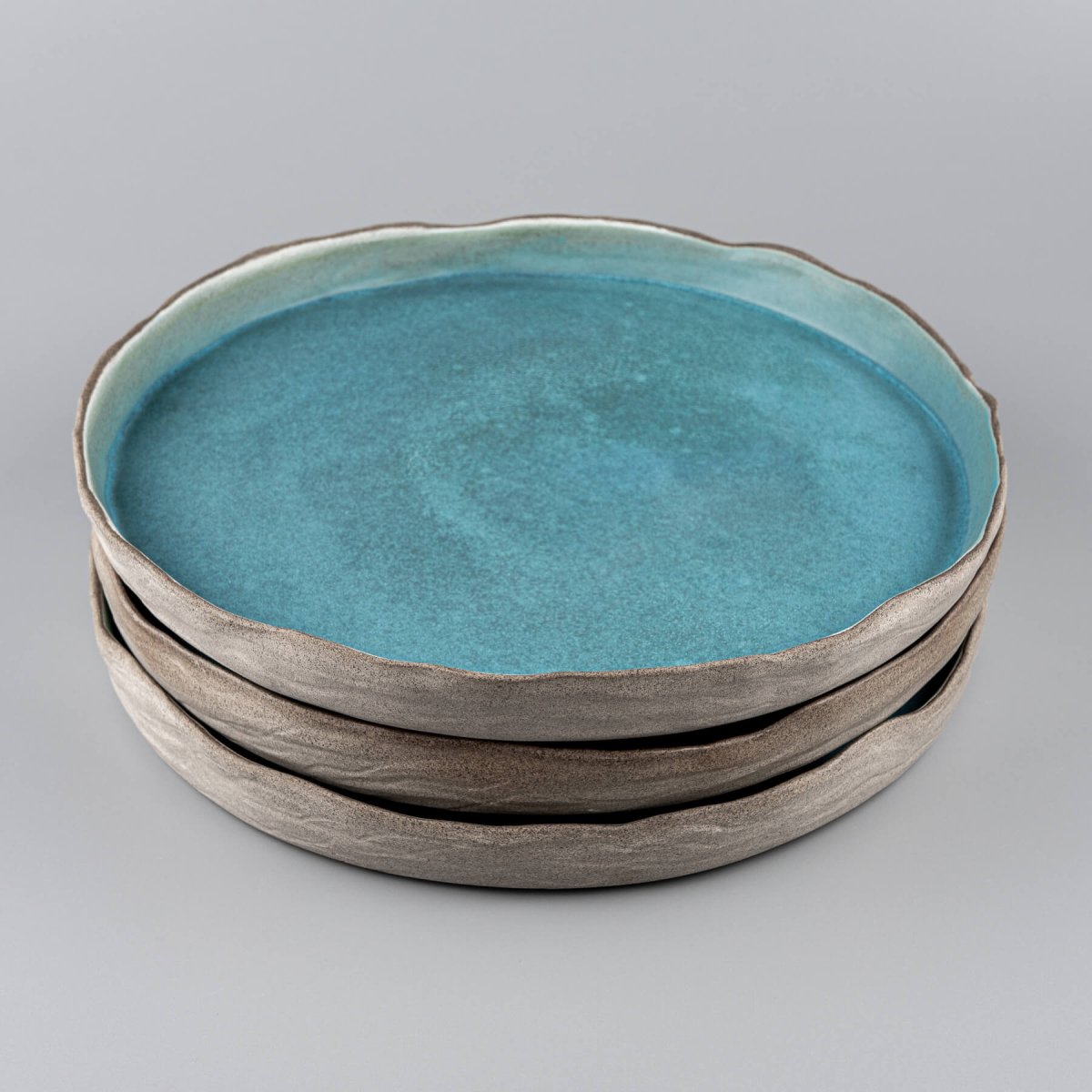 Stack of turquoise handmade dinner plates with refined edges for high-end dining.