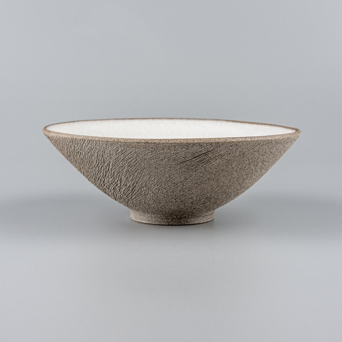 Handmade stoneware bowl with white matte glazed interior and raw carved exterior for restaurant plating.