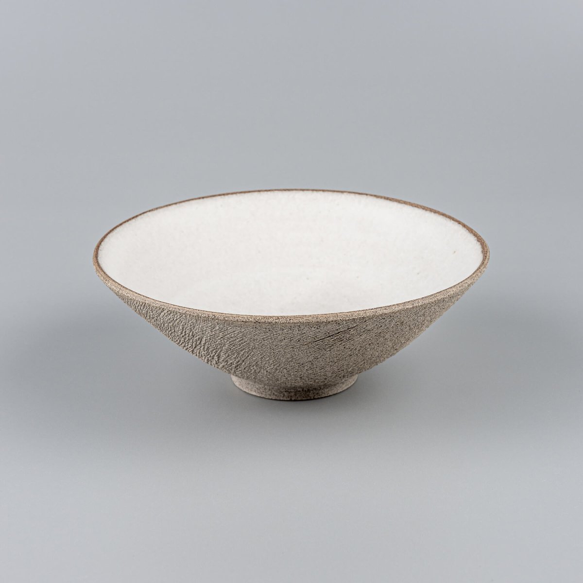 Elevated handmade ceramic bowl with carved brown exterior and glazed interior.