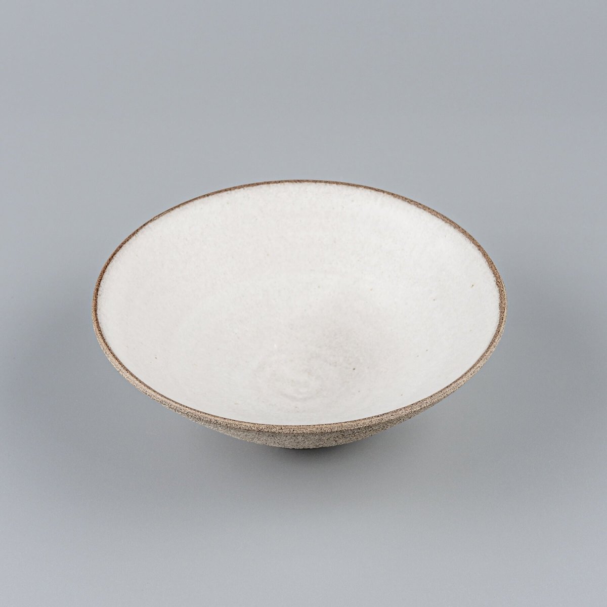 Elevated view of fine dining ceramic bowl with wide opening and footed base.
