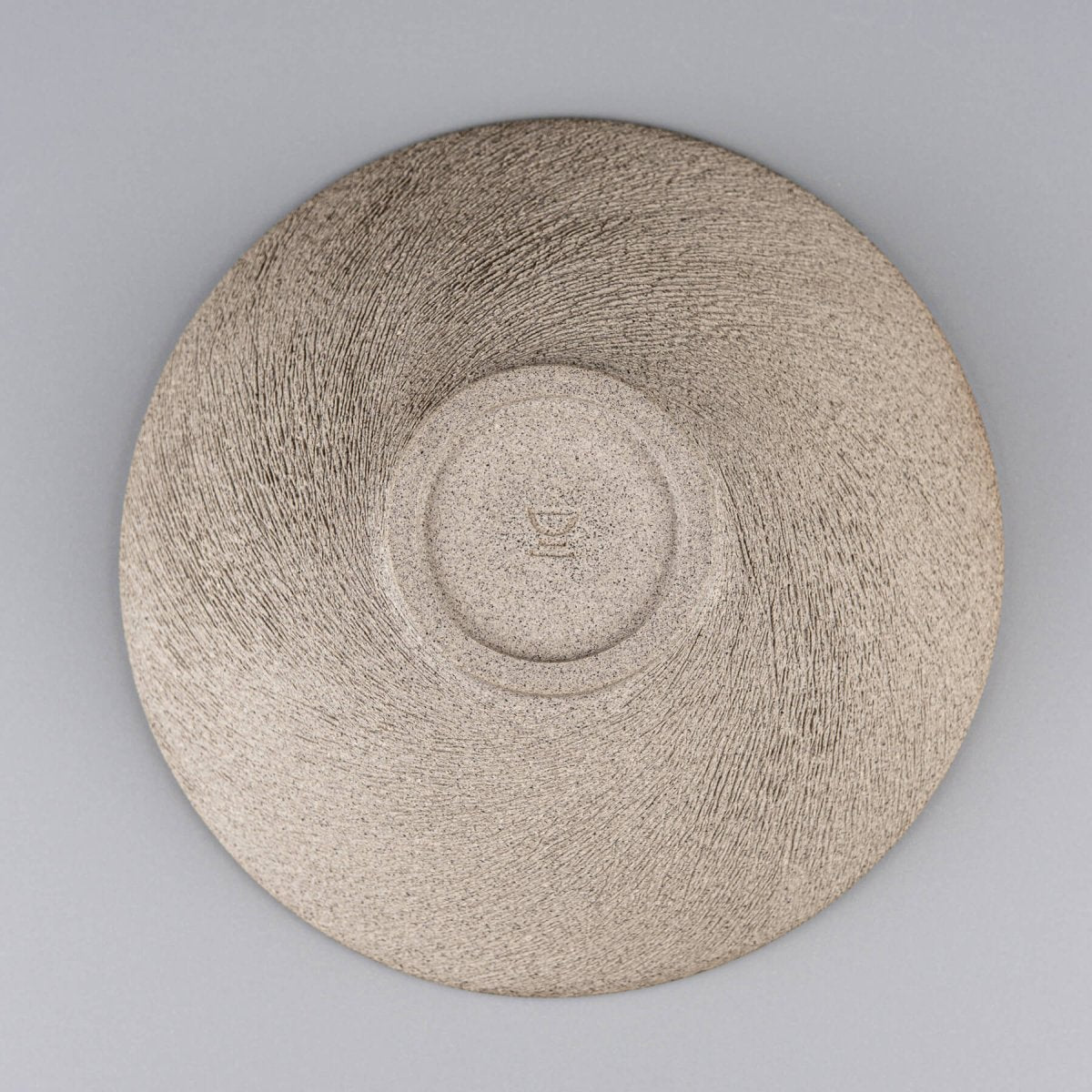 Underside of handmade bowl showing raw clay texture and potter’s signature.