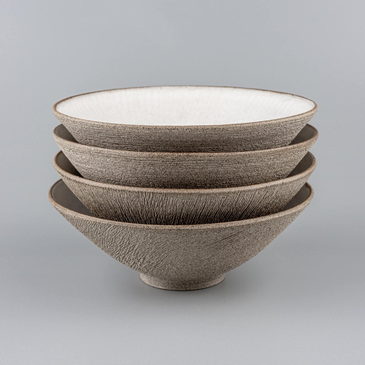 Handmade stoneware bowl set stacked together with carved texture and white matte interiors.