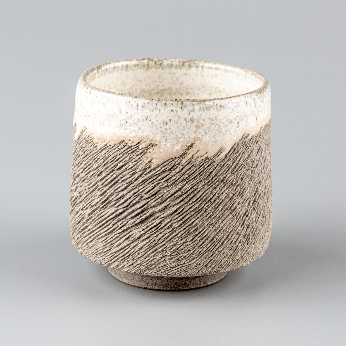 Rustic artisanal stoneware coffee cup with textured surface and white glazed rim, perfect for collectible pottery and decor.