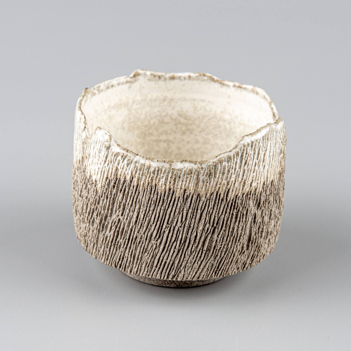 Artisan coffee cup in dark stoneware clay with irregular rim and tactile carved surface.