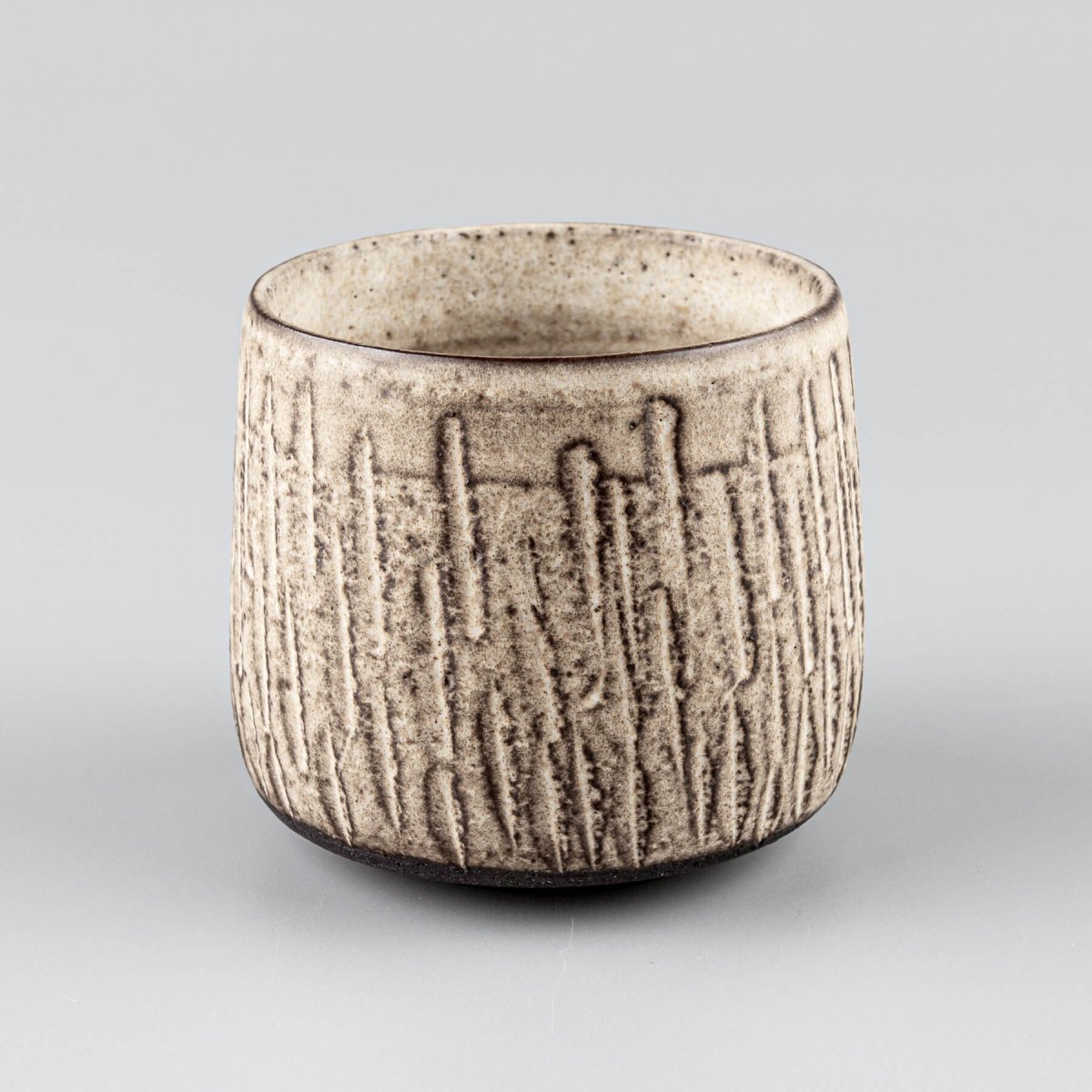 Handcrafted ceramic mugs with carved stoneware texture and matte glaze finish for modern tableware.
