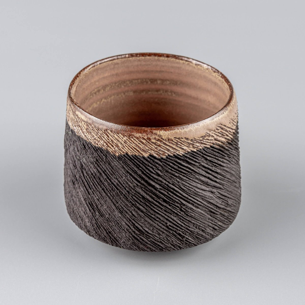 Handcrafted pottery mug in black stoneware with carved exterior and semi-gloss glazed rim, perfect for fine dining use.