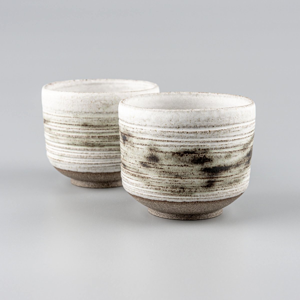 Handcrafted pottery mugs with white matte glaze and carved texture for modern tableware.