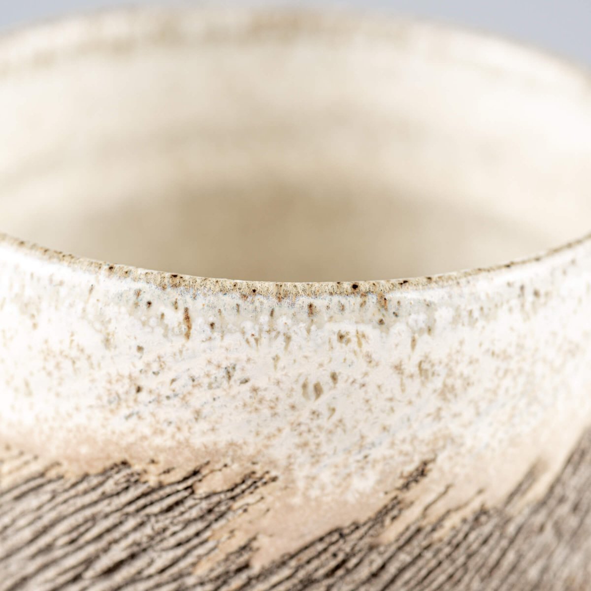 Detail of artisanal stoneware coffee cup exterior showing unique tactile carving and ceramic artistry for tableware.
