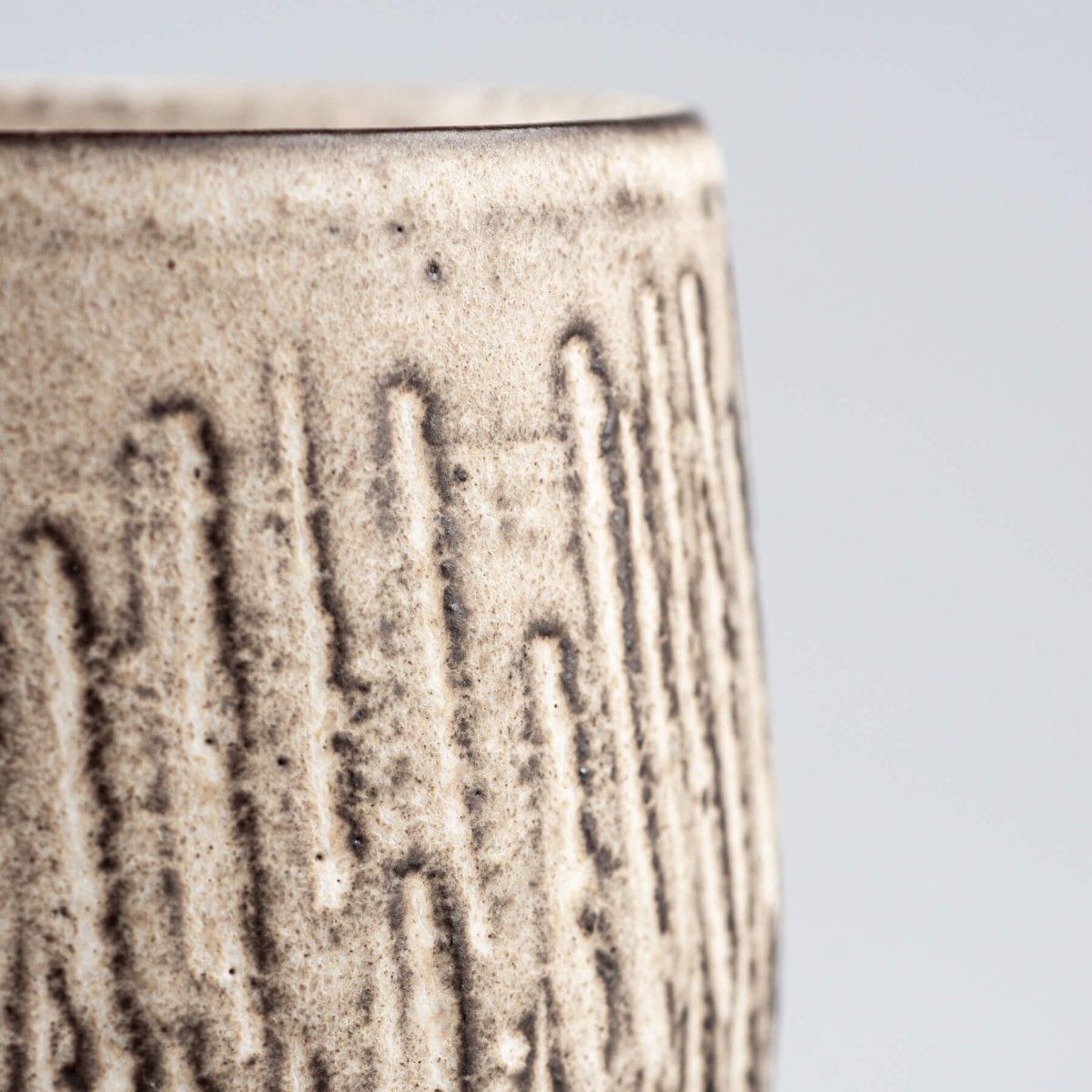 Detail of carved stoneware mugs exterior with textured vertical pattern and artisan glaze.