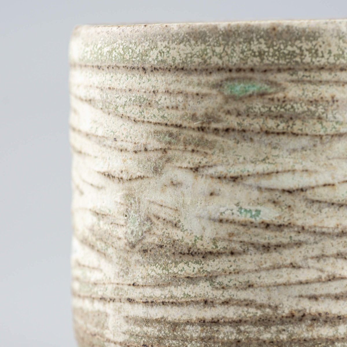 Close-up of handcrafted ceramic mug with detailed carving and rustic matte finish.
