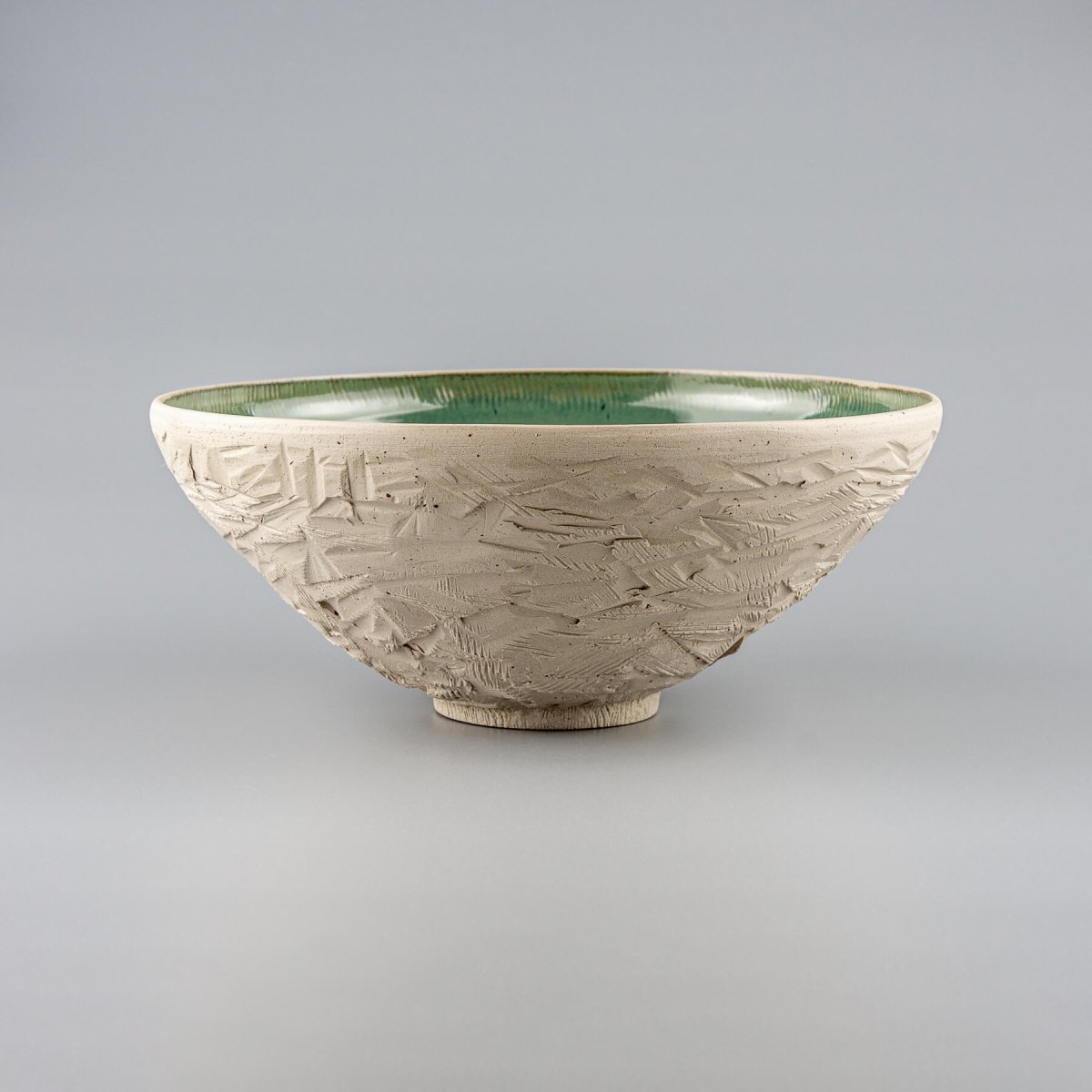 Front view of ceramic serving bowl with carved white stoneware exterior and glossy green interior.