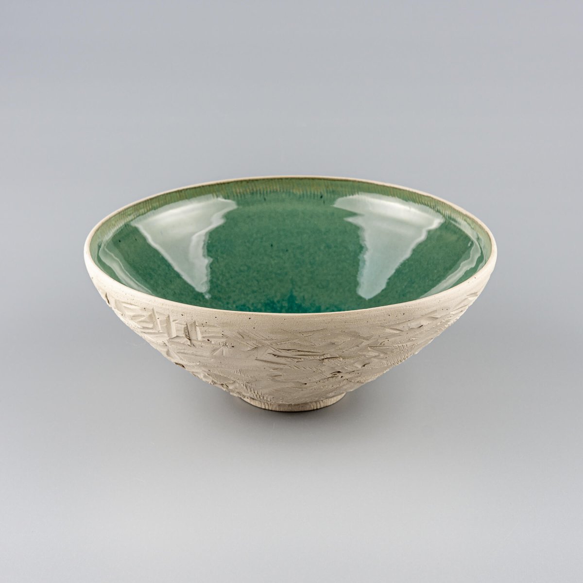Angled side view of handmade ceramic serving bowl with textured unglazed exterior and rounded rim.