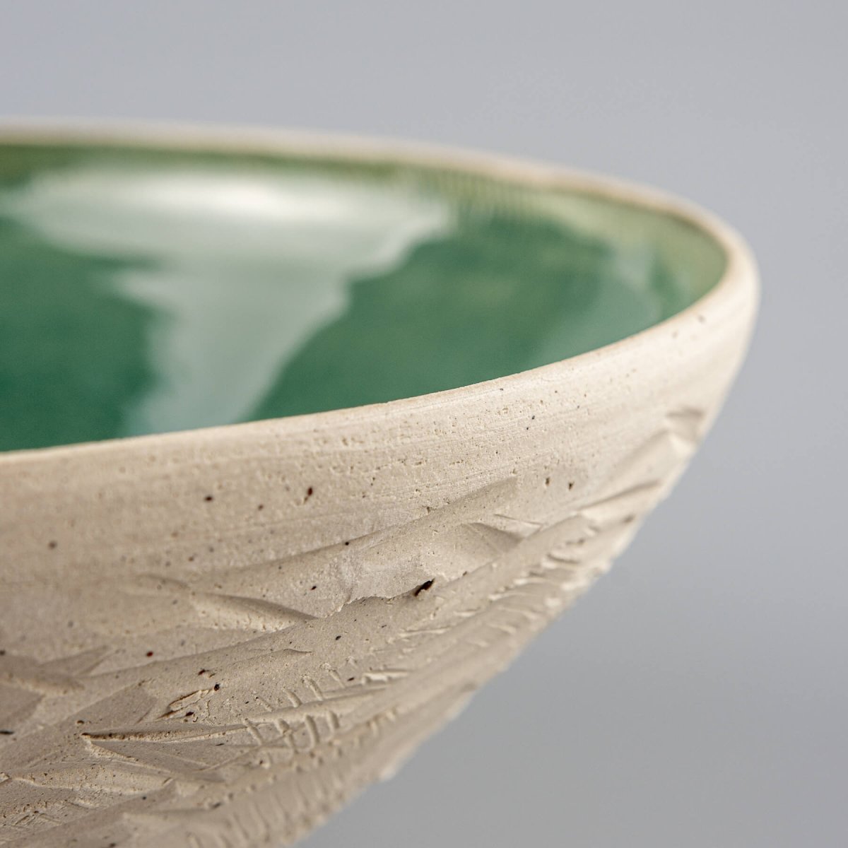 Zoomed-in corner of ceramic bowl showing glaze edge and carved outer wall.