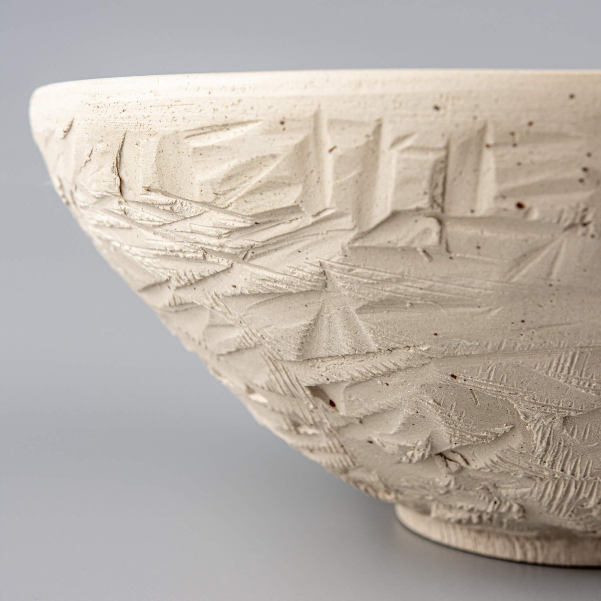 Side view of carved ceramic serving bowl with textured unglazed white stoneware exterior.