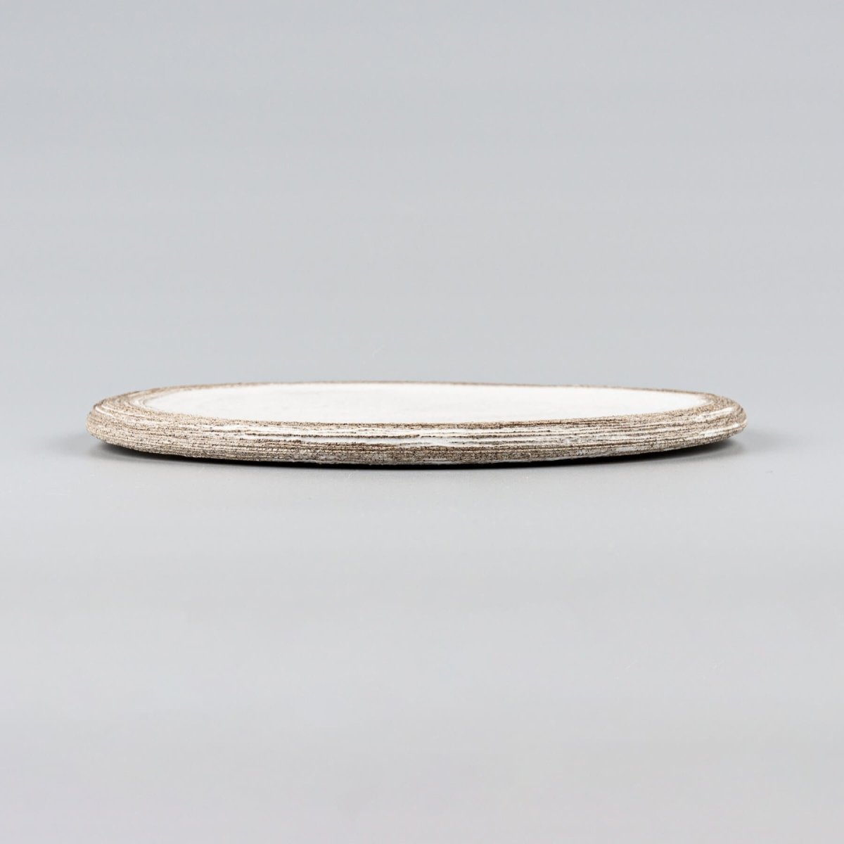 Side view of a luxury handmade ceramic plate in matte white finish over dark clay.