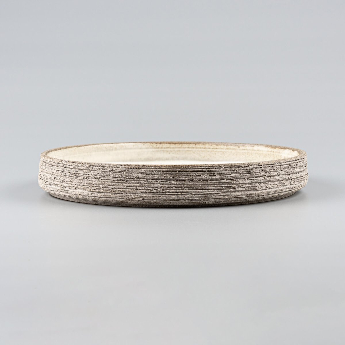 Handmade stoneware plate with raw textured exterior and smooth glazed interior.