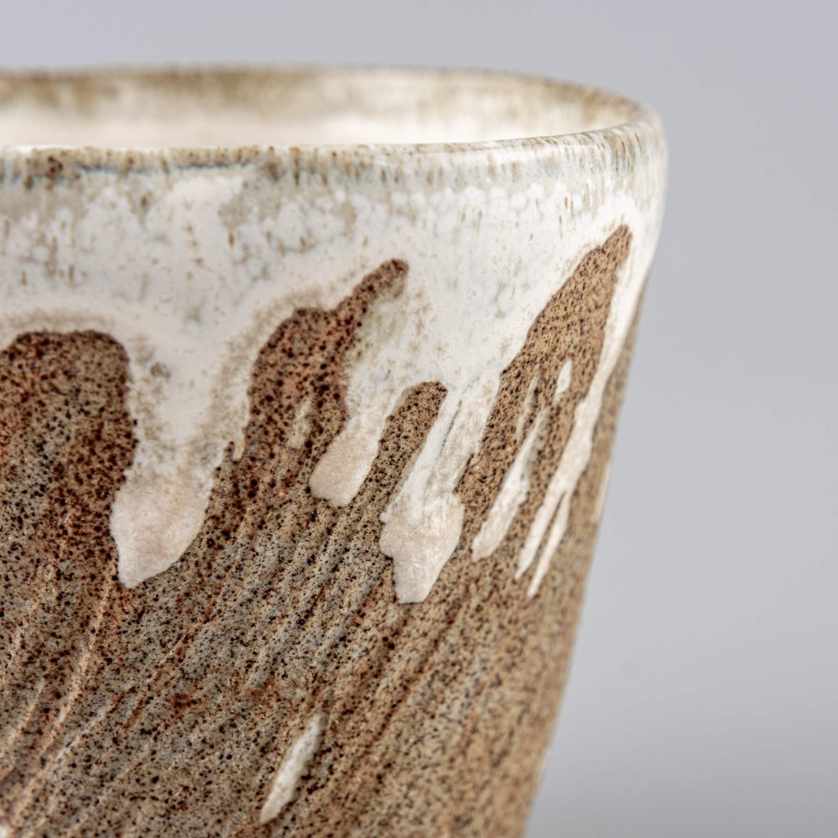 Detailed side of ceramic espresso mug with flowing glaze over textured clay.