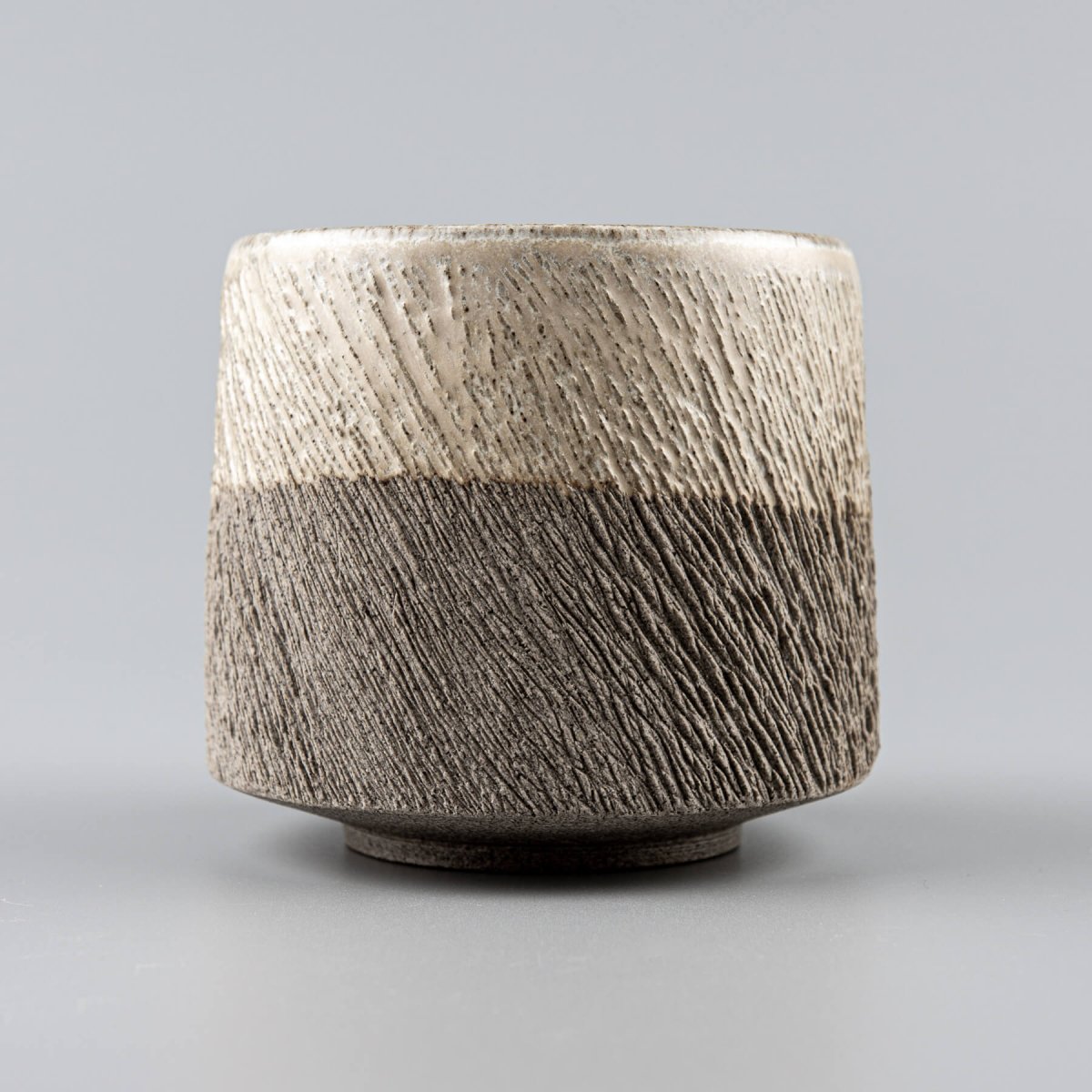 Detail of textured stoneware pottery coffee mug with partially glazed surface for modern design.