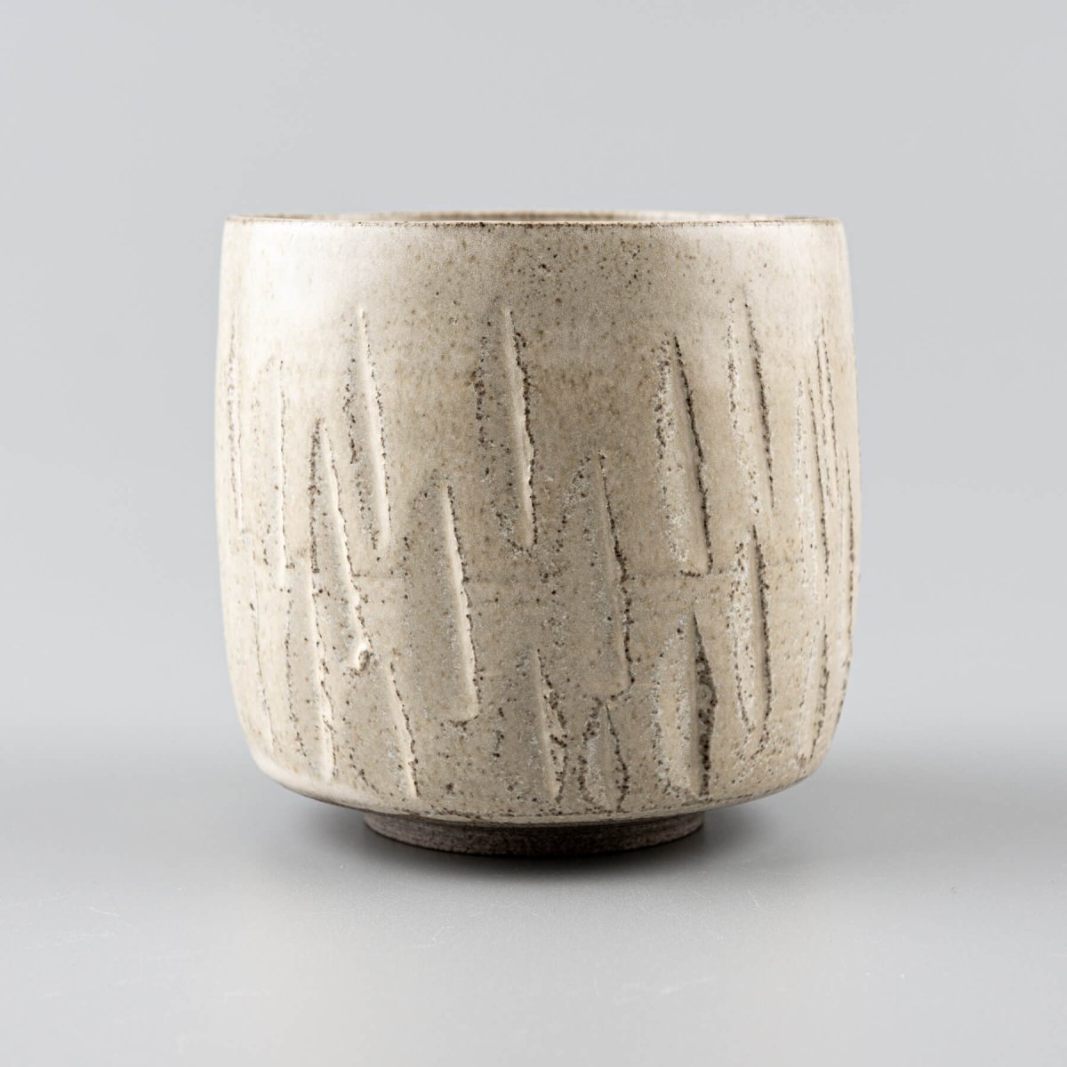 Side view of a ceramic handmade cup with textured carvings and artisanal glaze.