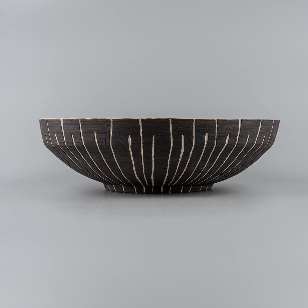 Side profile of a handcrafted decorative stoneware bowl with elegant beveled shape.