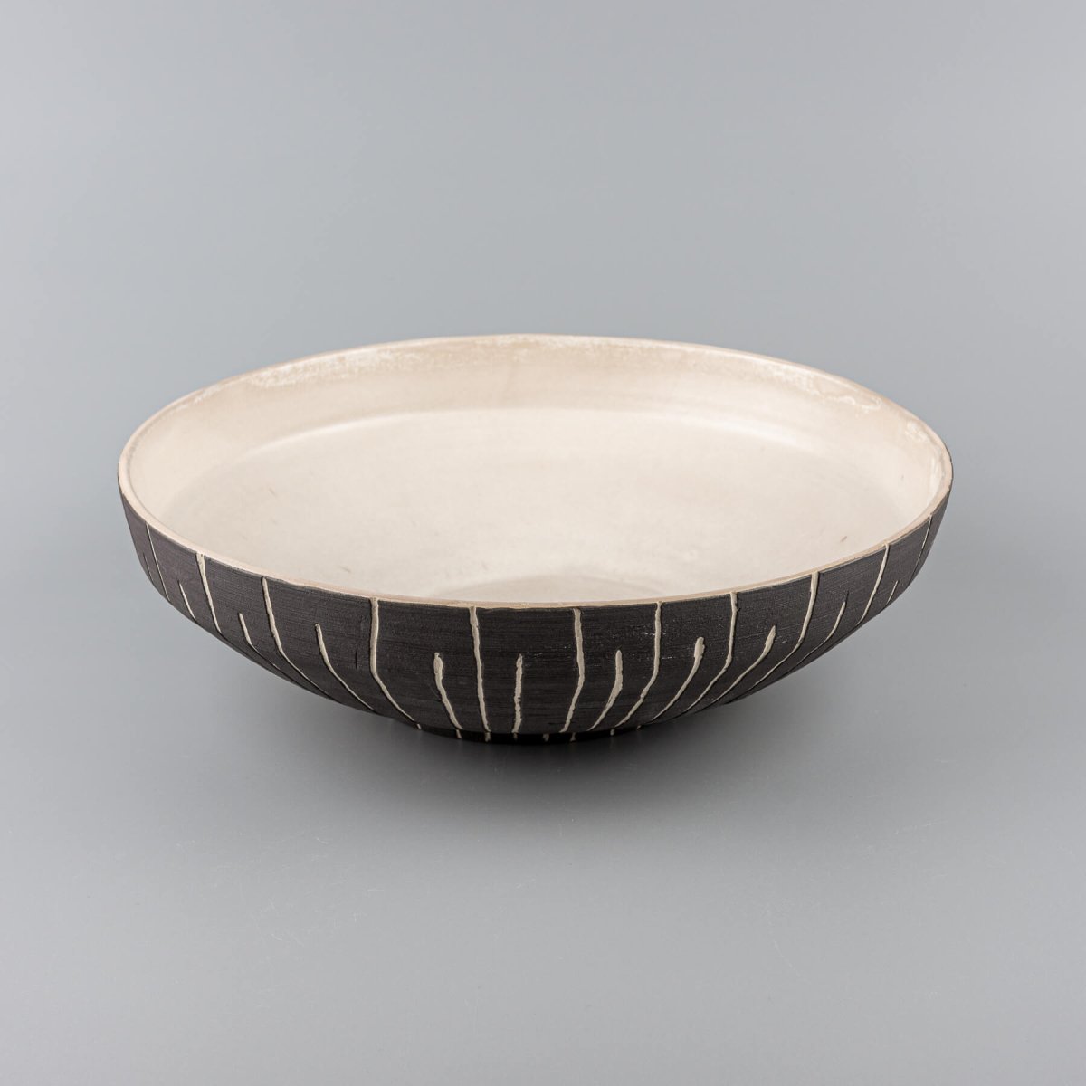 Angled view of a handmade bowl showing contrast between matte interior and carved slip exterior.