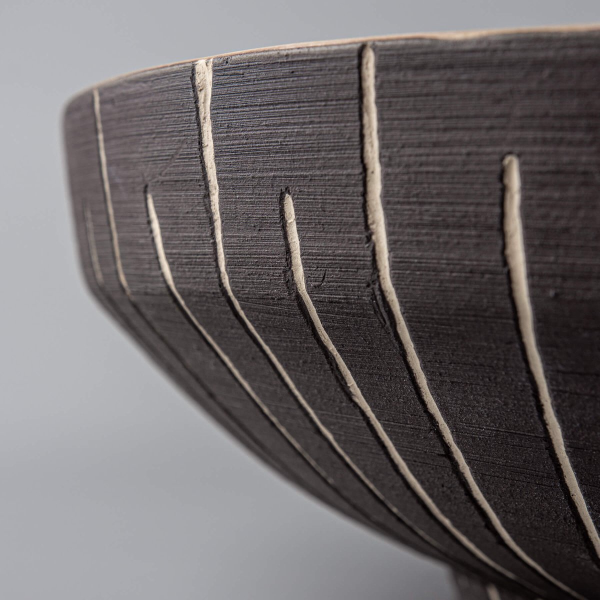 Detail of carved vertical slip lines on dark exterior of artisan decorative bowl.