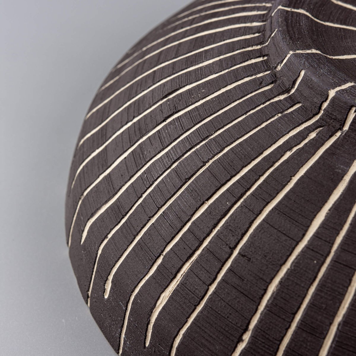 Angled texture view of slip-carved lines on unglazed dark stoneware.