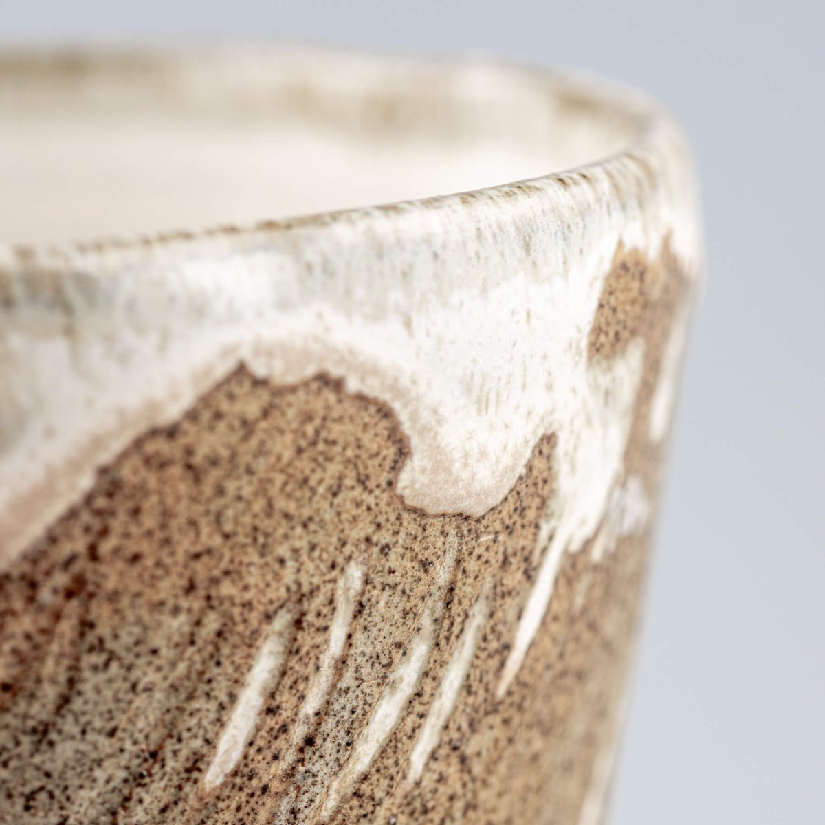 Close-up detail of ceramic espresso mug rim with flowing white glaze over textured stoneware.