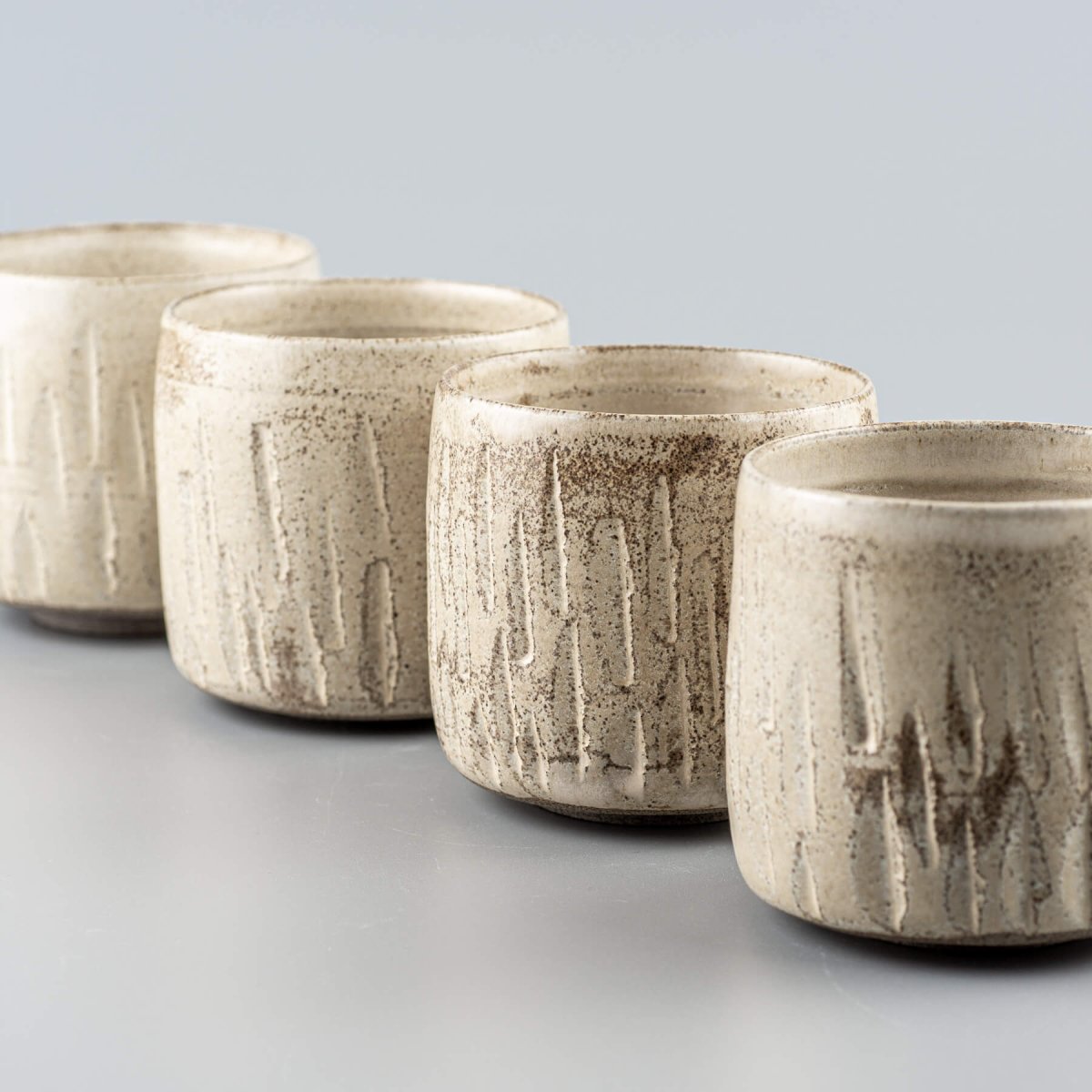 Four ceramic handmade cups aligned with matte finish and carved stoneware texture.