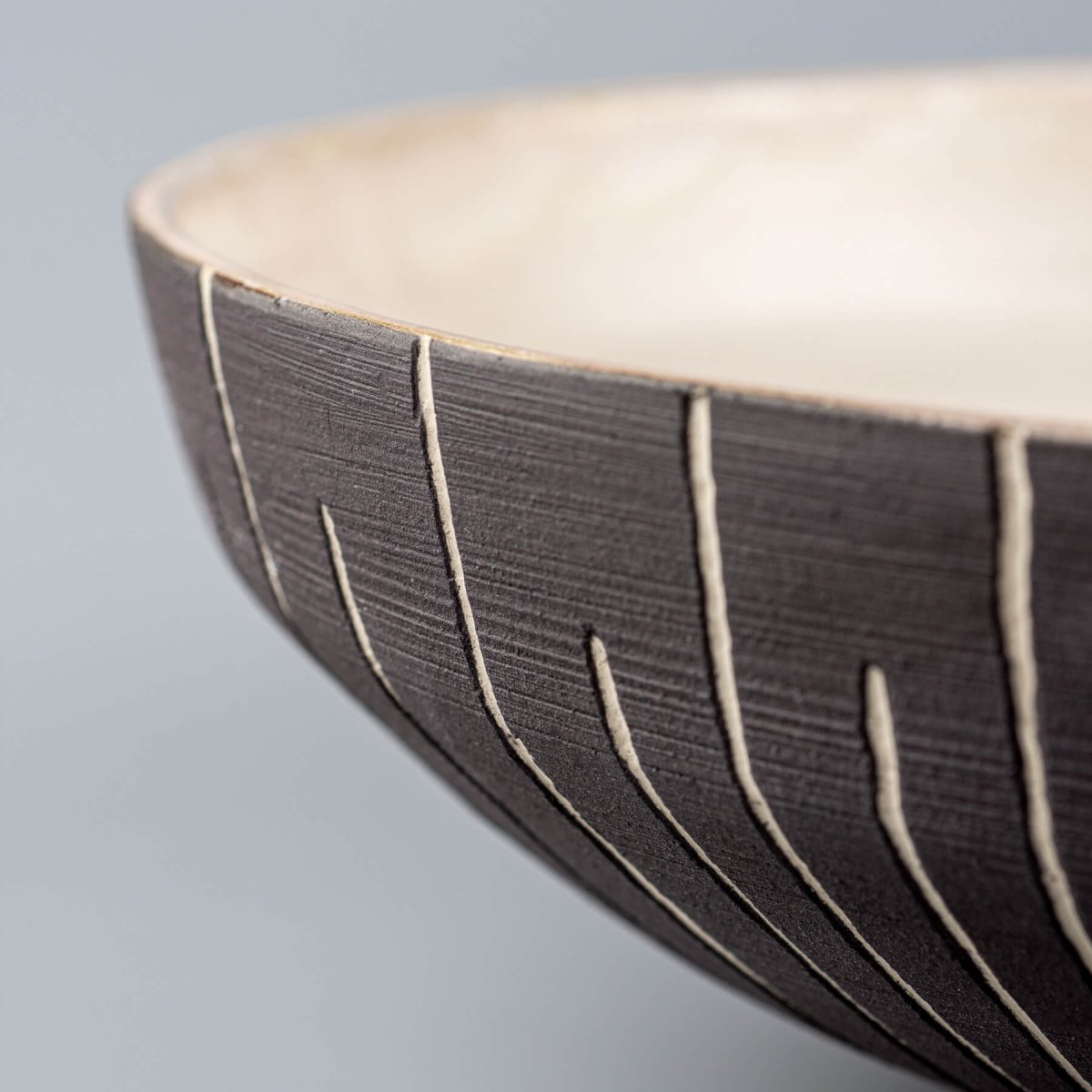 Side detail of vertical carving on handmade ceramic bowl’s exterior surface.