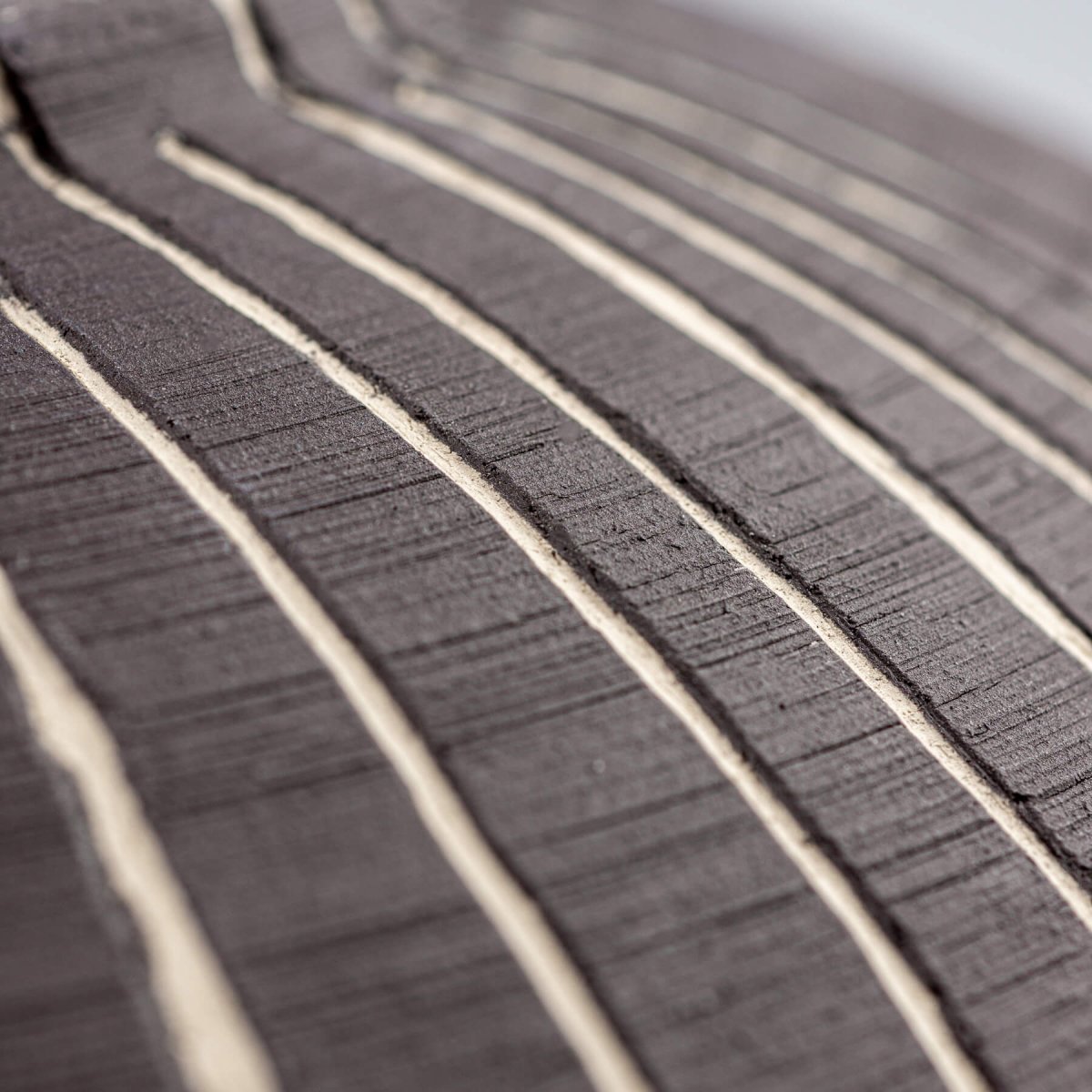 Artisan ceramic texture detail emphasizing hand-drawn carved linear pattern.