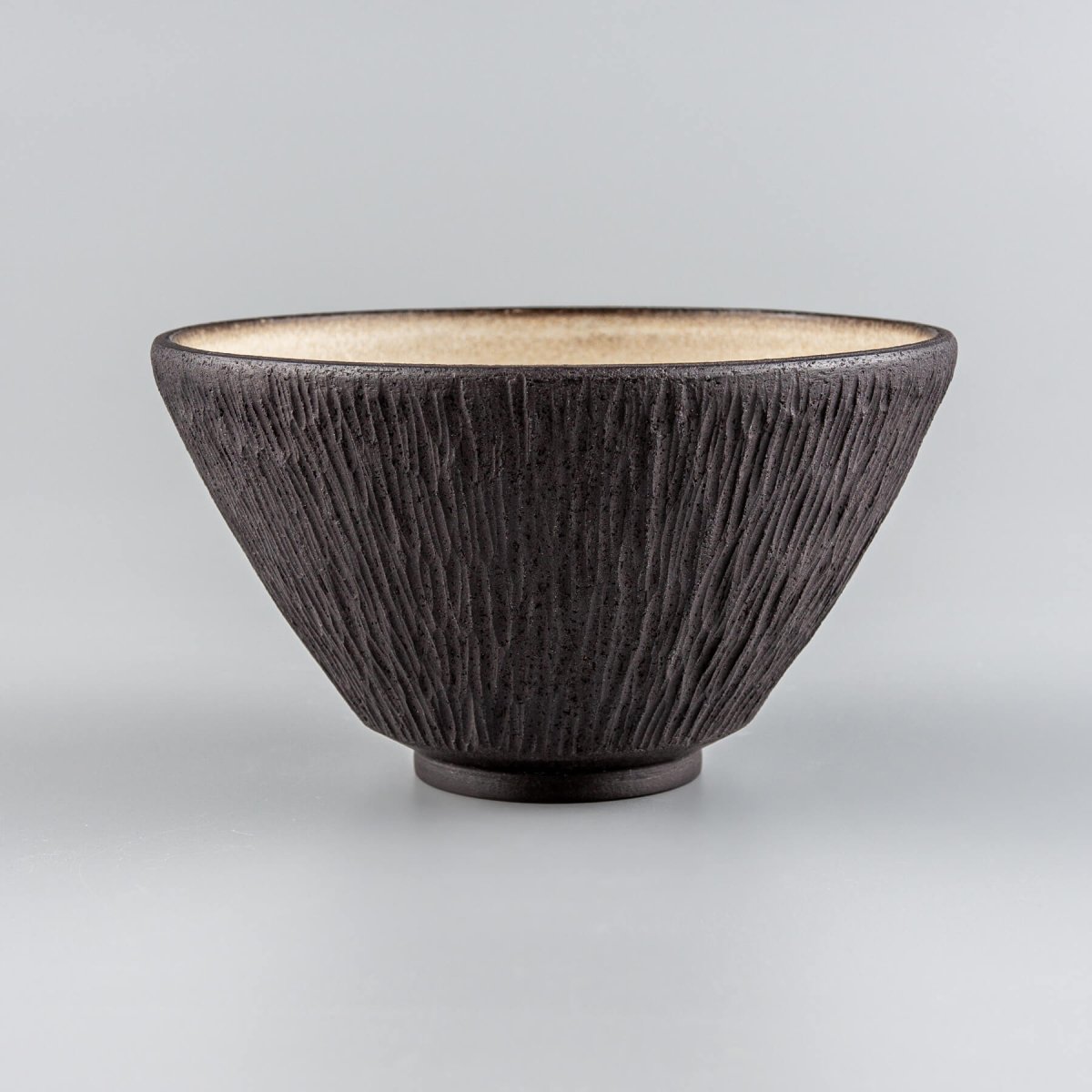 Handmade stoneware bowl with carved black exterior and beige glazed interior, ideal for luxury dining.
