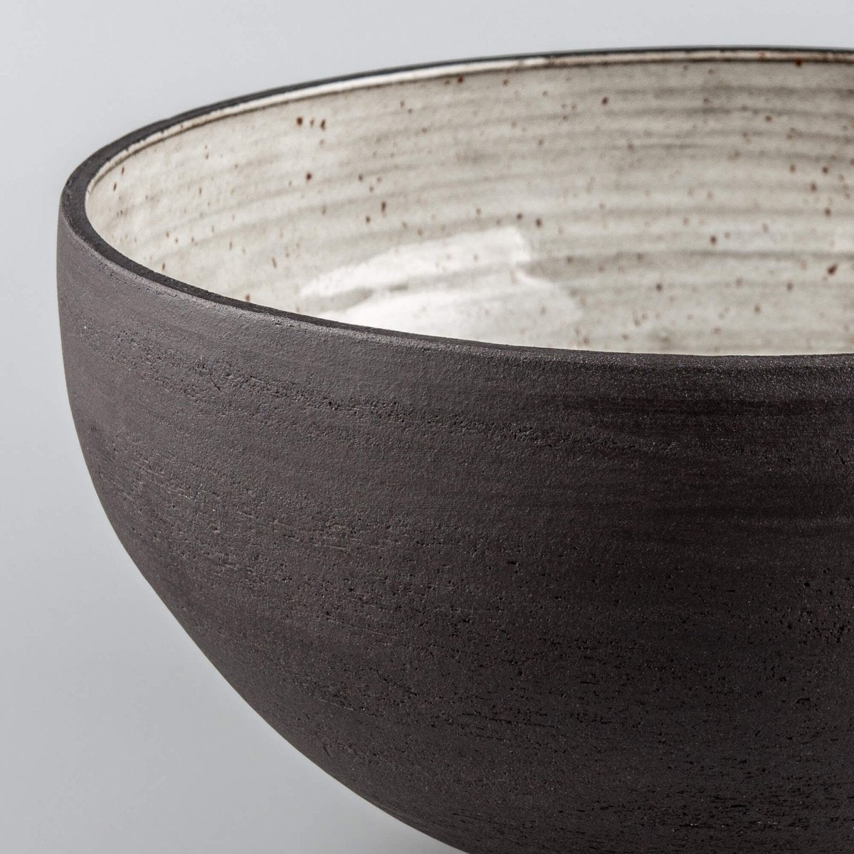 Close-up of handmade serving bowl with glossy cream glaze, dark rim, and speckled handmade ceramic detail.