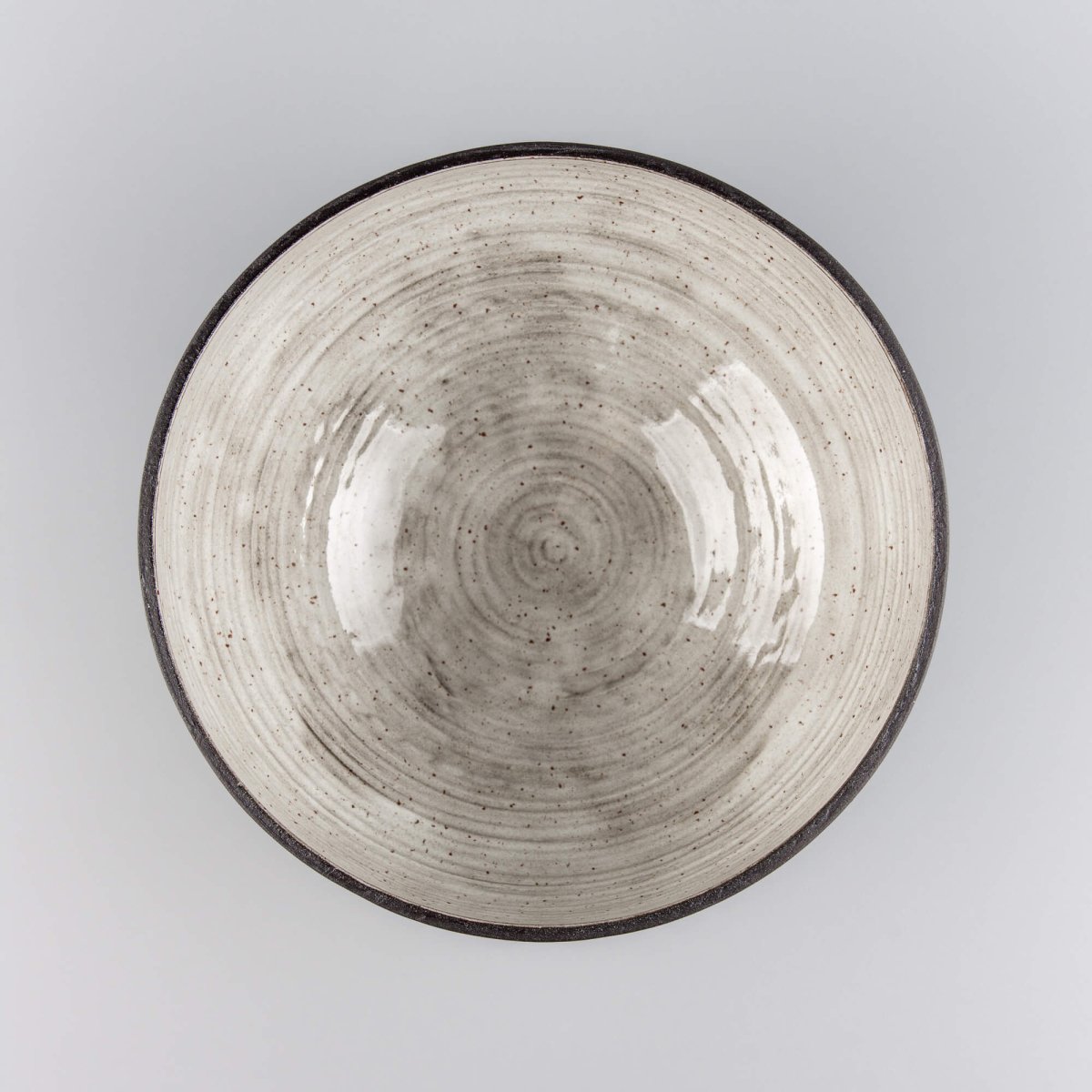 Handmade serving bowl with wide handmade form, dark clay exterior, and glossy speckled interior for tableware.