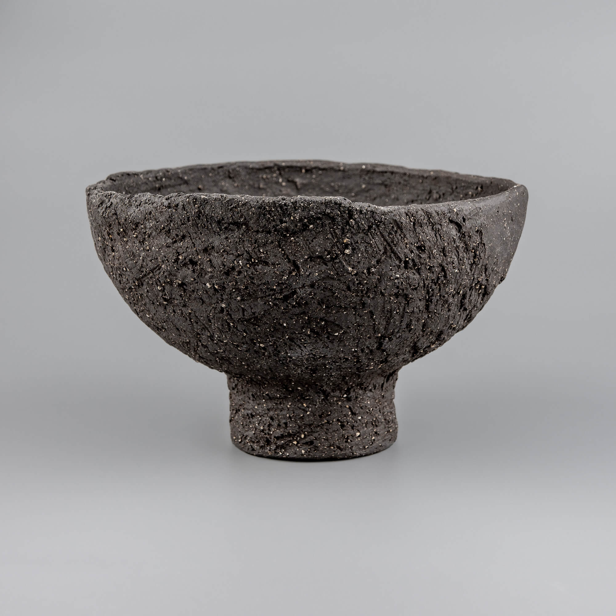 Handmade decorative bowl with rough black ceramic texture, elevated foot, and sculptural form for boutique hotel decor.