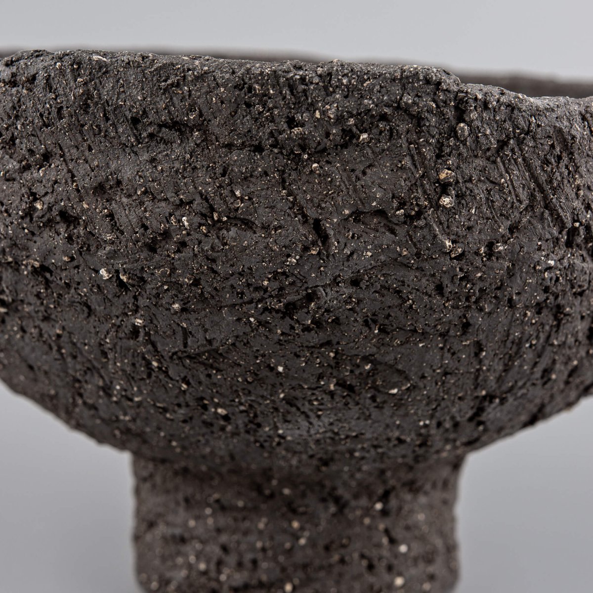 Side detail of handmade decorative bowl with organic rim, dark stoneware texture, and boutique hotel interior appeal.