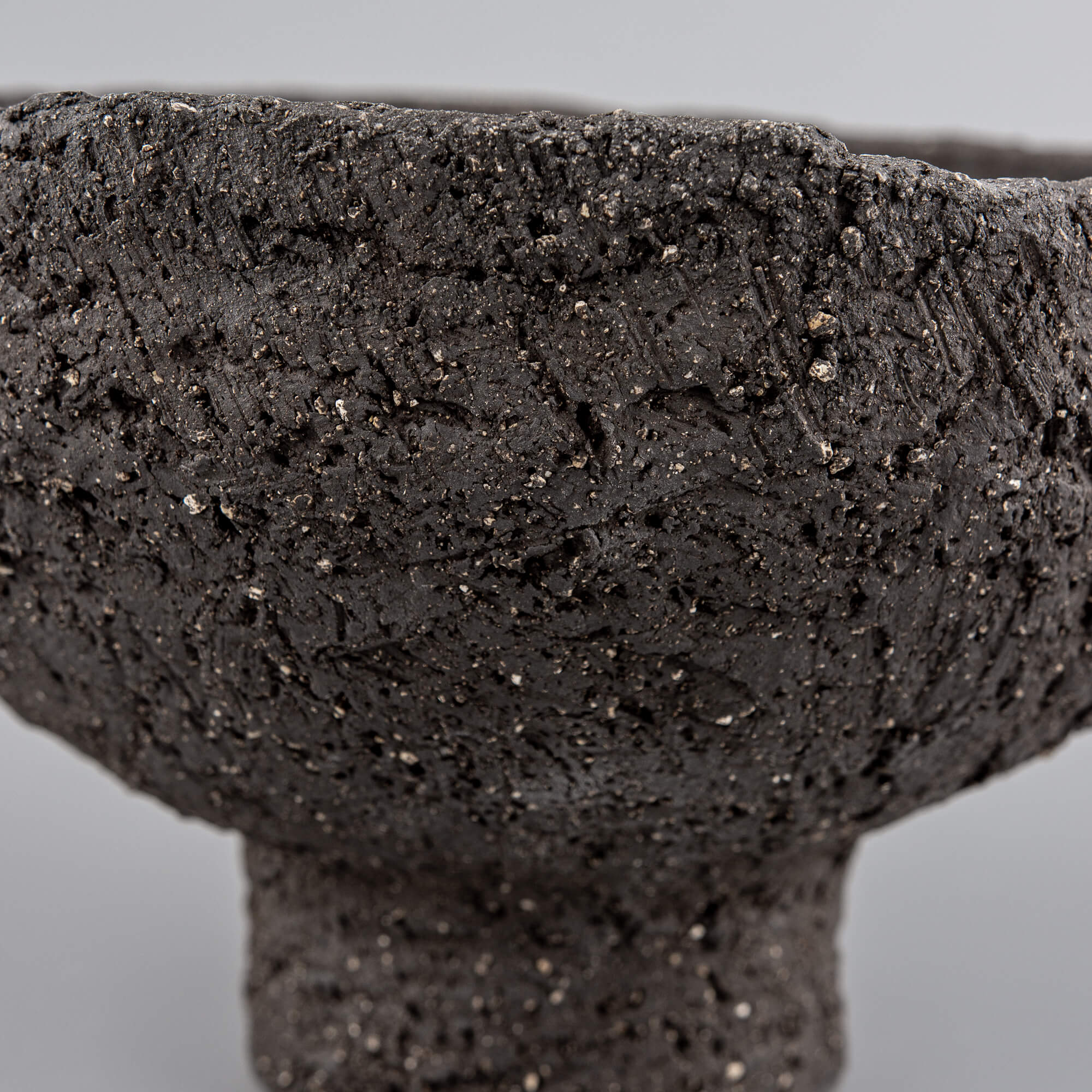 Side detail of handmade decorative bowl with organic rim, dark stoneware texture, and boutique hotel interior appeal.