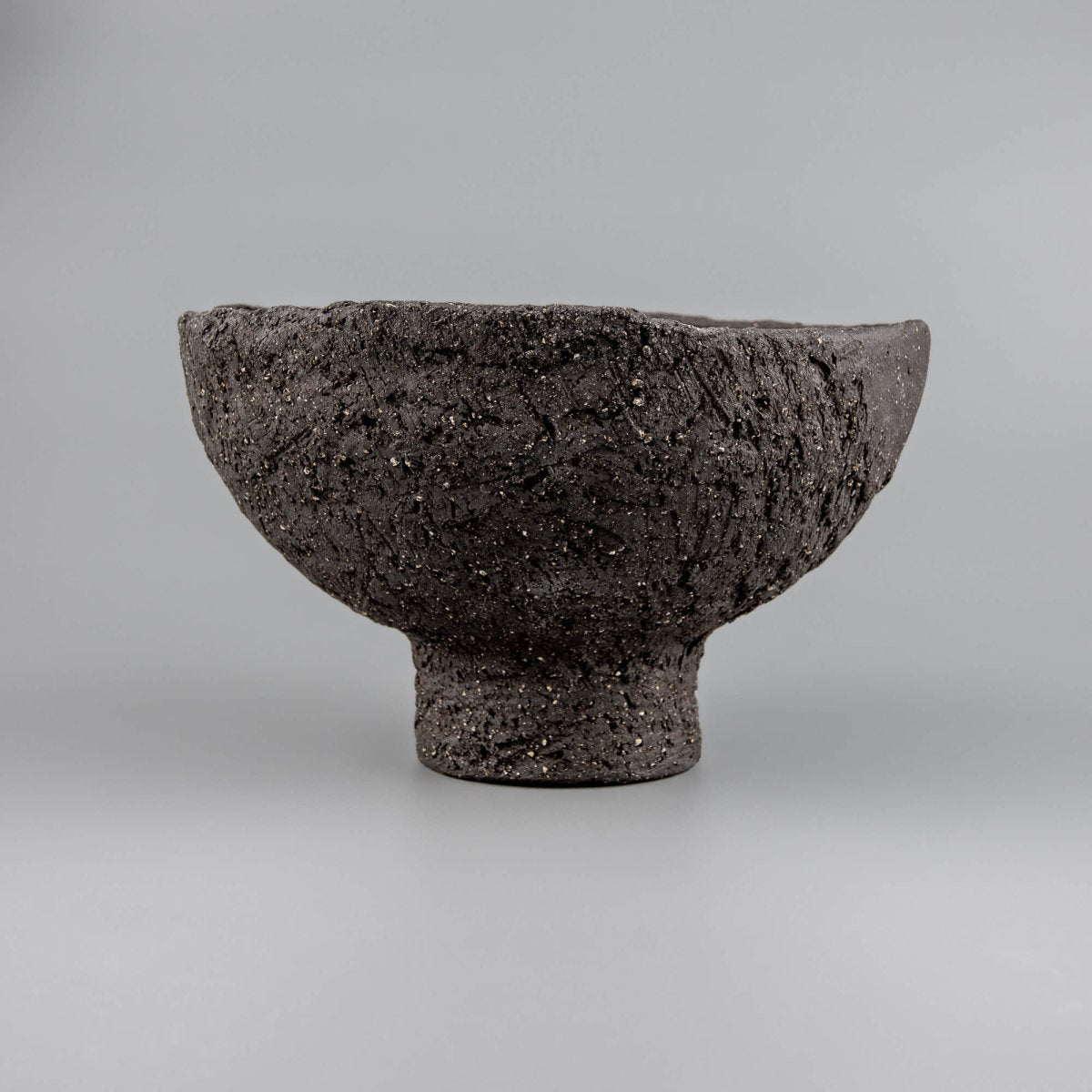 Textured handmade decorative bowl with black clay surface, pedestal base, and bold presence for home or hotel interiors.
