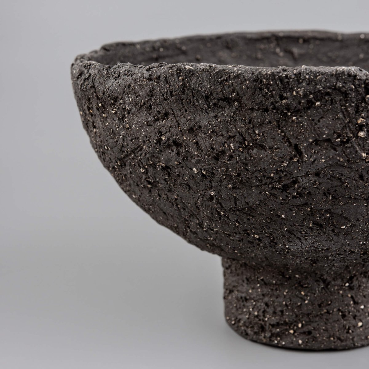 Close-up of handmade decorative bowl with rough black ceramic surface, mineral speckles, and artisan texture detail.