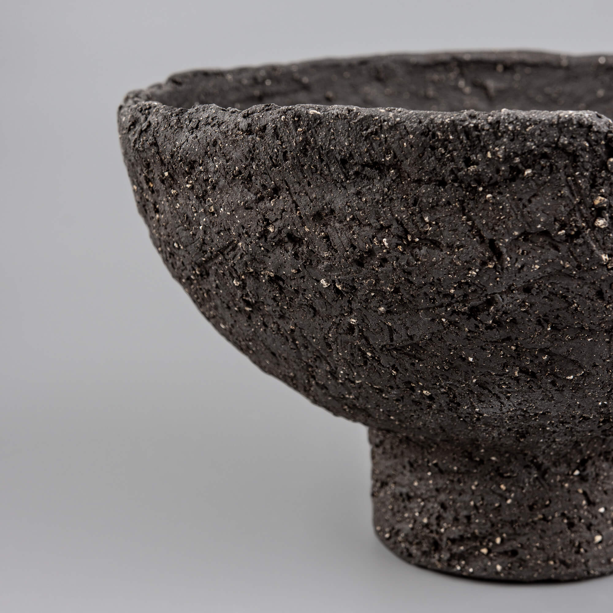Close-up of handmade decorative bowl with rough black ceramic surface, mineral speckles, and artisan texture detail.