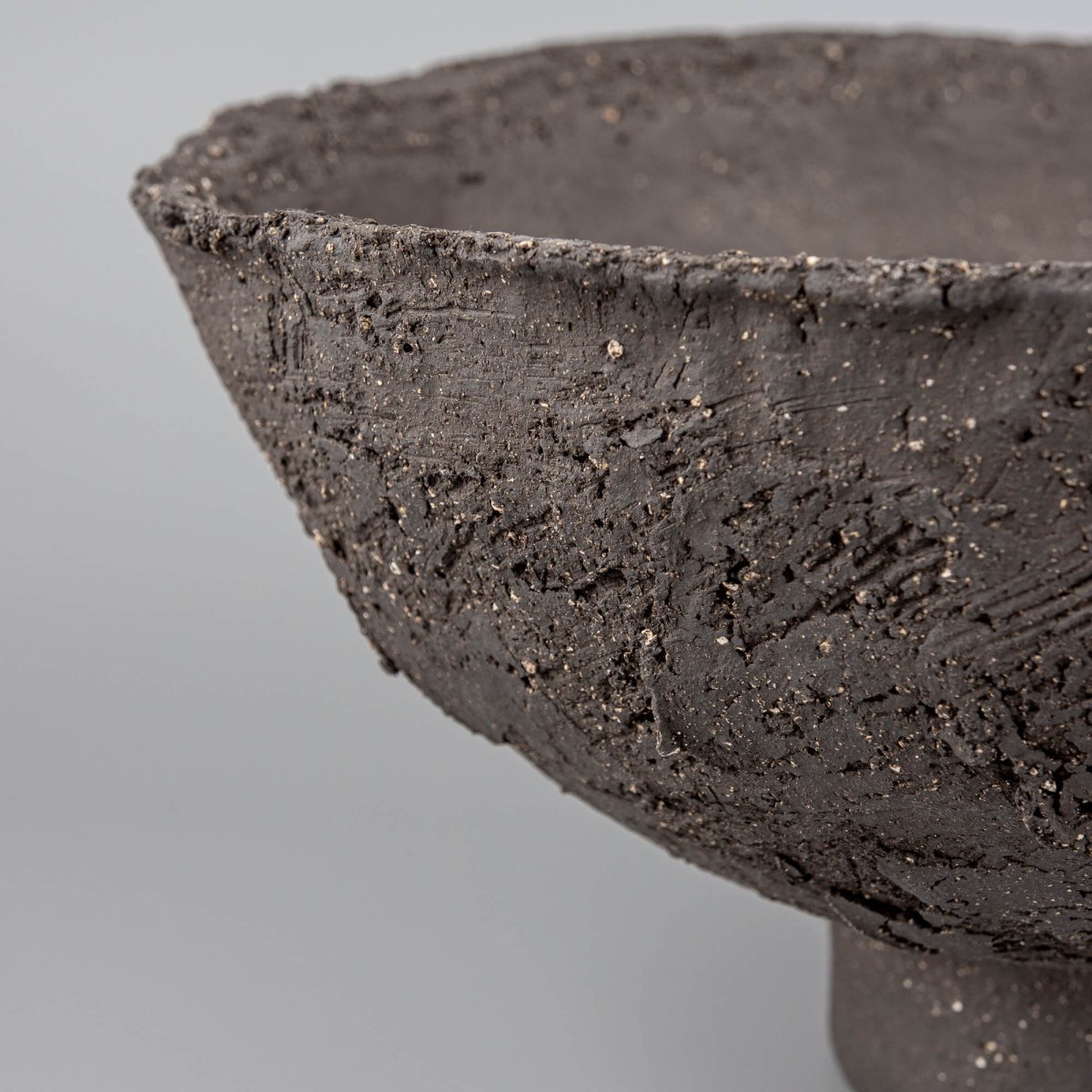 Handmade decorative bowl close-up showing rough stoneware texture, mineral speckles, and artisan ceramic surface.